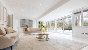 A spacious living room with a beige sofa, a round coffee table, and large windows offering a view of the outdoors.