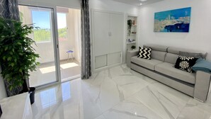 A modern living room with a sofa, a coffee table, a potted plant, and a sliding glass door leading to a balcony.