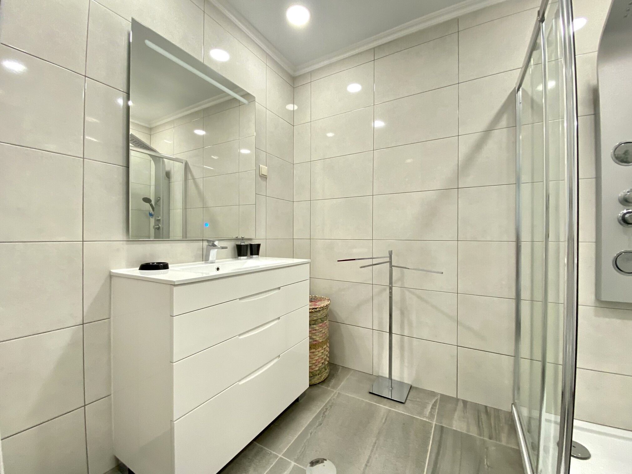 A modern bathroom with a white vanity, a large mirror, and a glass shower enclosure.