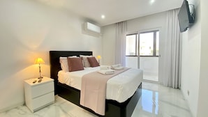 A modern hotel room with a large bed, bedside tables, a flat-screen TV, and a balcony with curtains.