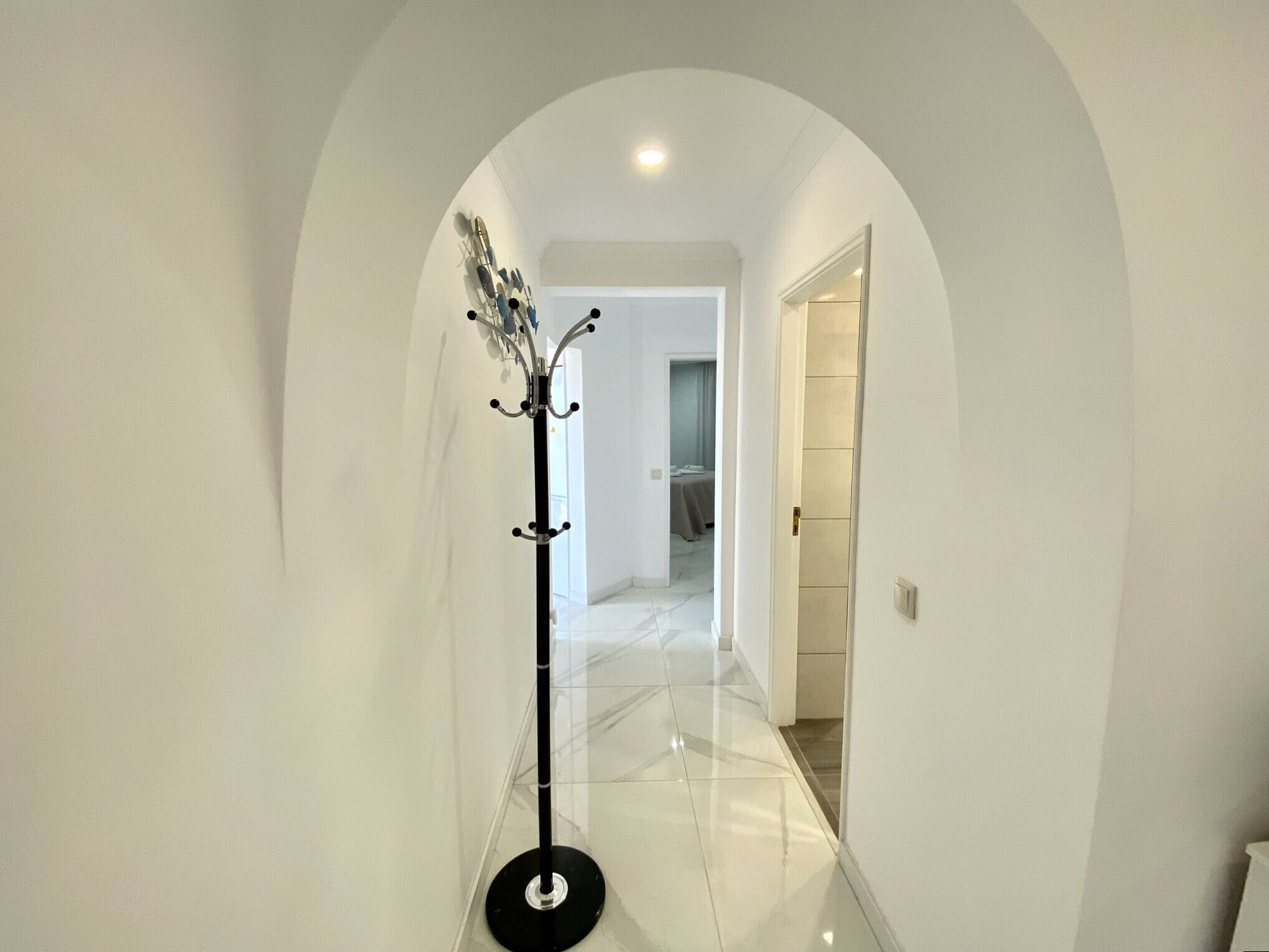 A hallway with a coat rack, a door leading to a room, and a tiled floor.