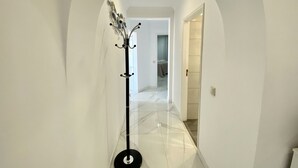 A hallway with a coat rack, a door leading to a room, and a tiled floor.