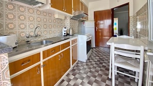 A compact kitchen with wooden cabinets, a white countertop, a sink, a stove, and a refrigerator. - Quarteira Beach Apartment by Homing (Loulé)