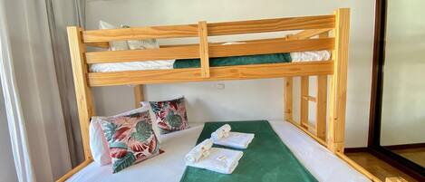 A bunk bed with a green blanket and tropical pillows, an air conditioning unit, and a window with wooden frames.
