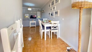 A modern living space with a dining area, a kitchen, and a TV in the background. - Quarteira Beach Apartment by Homing (Loulé)