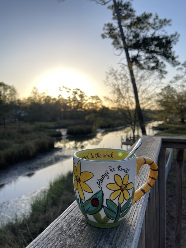 A mug with floral designs and a quote on a wooden surface near a river.