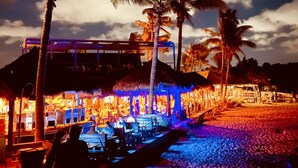 Un resort sulla spiaggia con strutture a tetto di paglia, palme e una zona piscina.