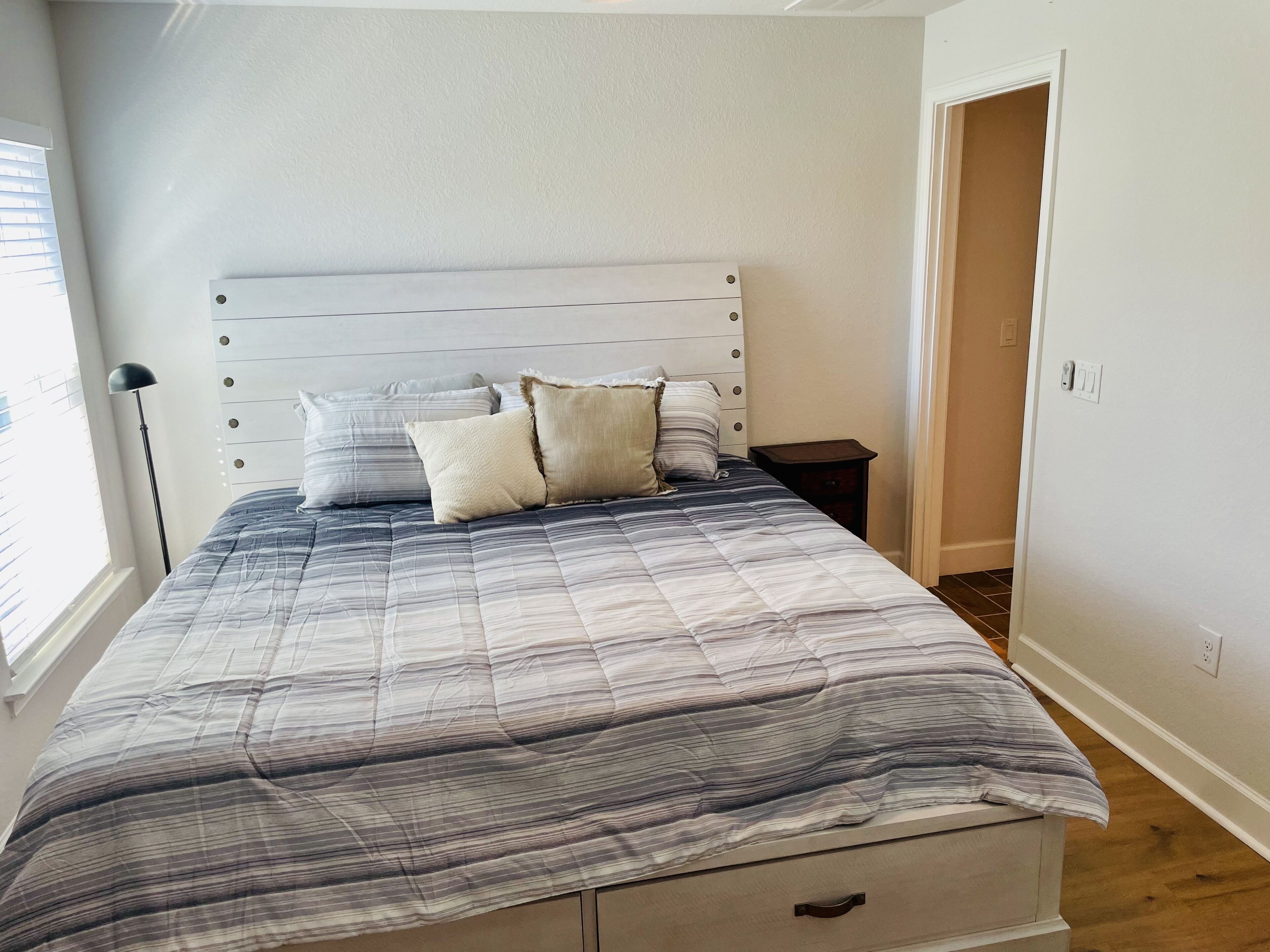 A bedroom with a bed, a nightstand, a lamp, and a door.