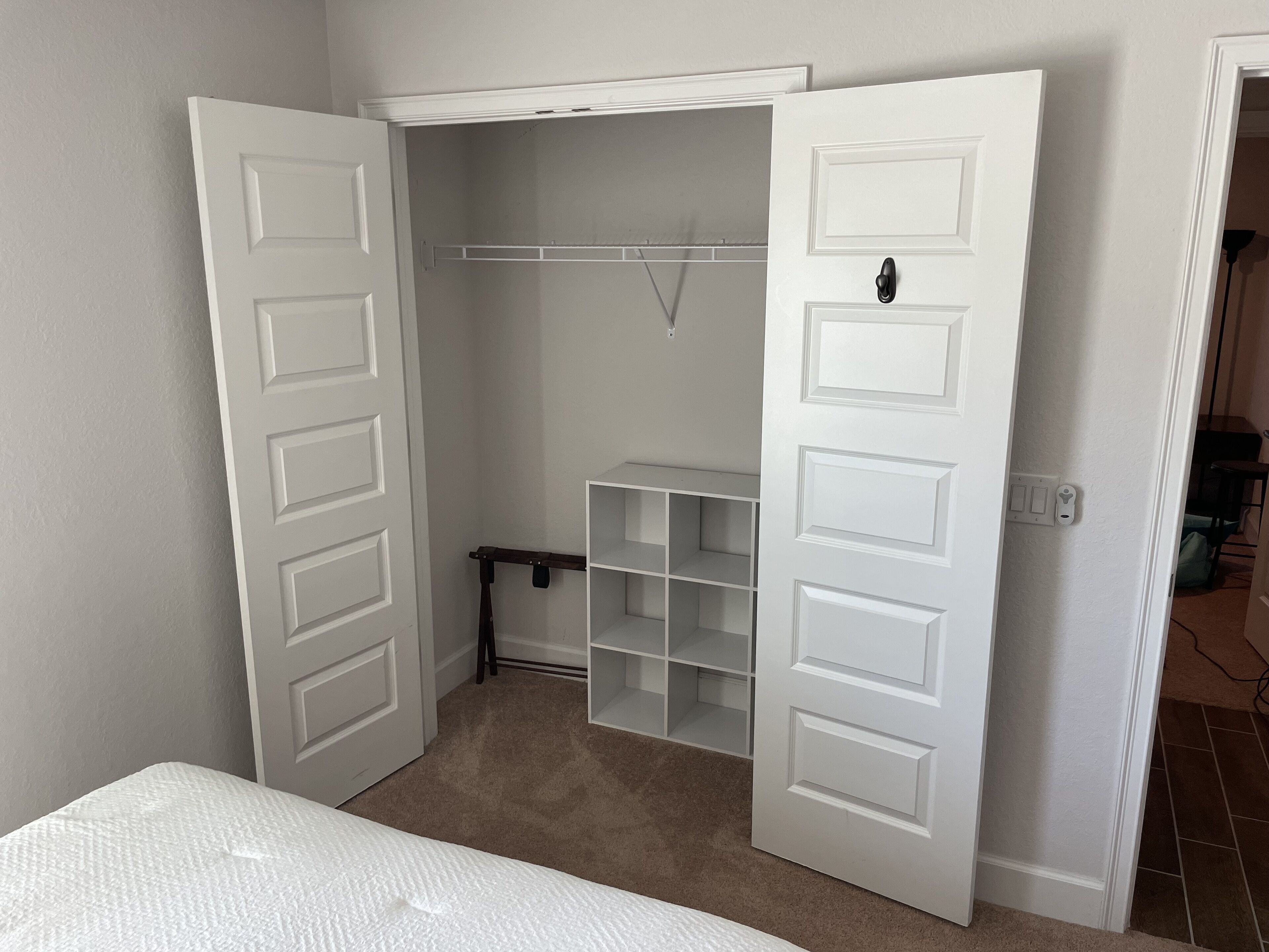 A walk-in closet with white doors, a hanging rod, and open shelving.