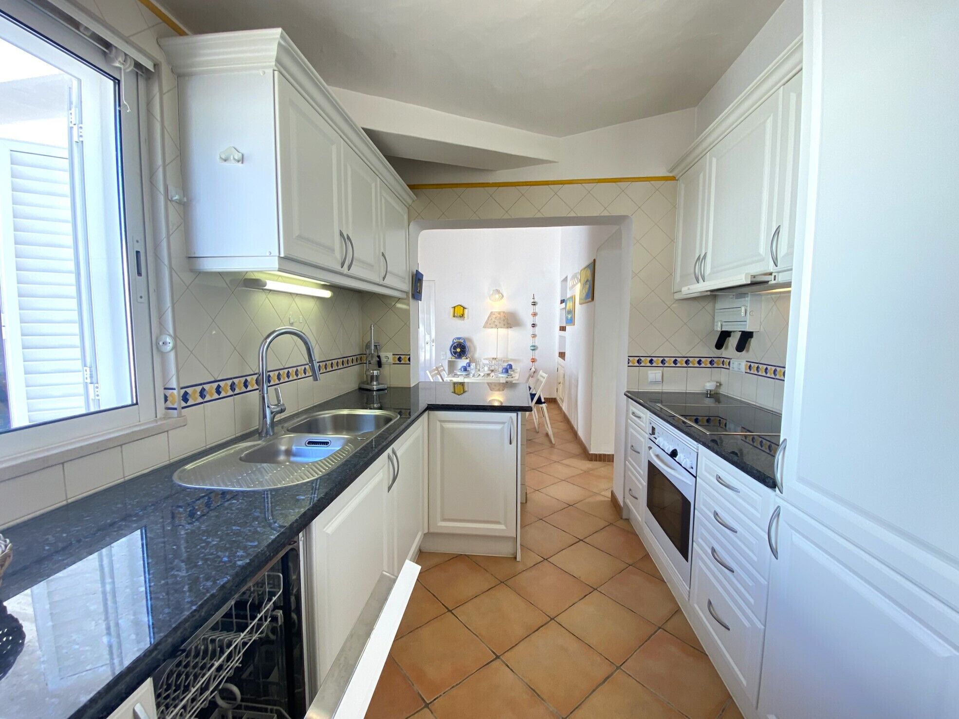 Cucina con mobili bianchi, piano di lavoro nero e pavimento piastrellato.