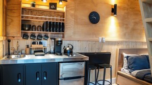 Una cocina compacta con lavamanos, hervidor, cafetera y armarios.