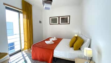 A hotel room with a bed, a bedside table with a lamp, a window with curtains, and two framed pictures on the wall.