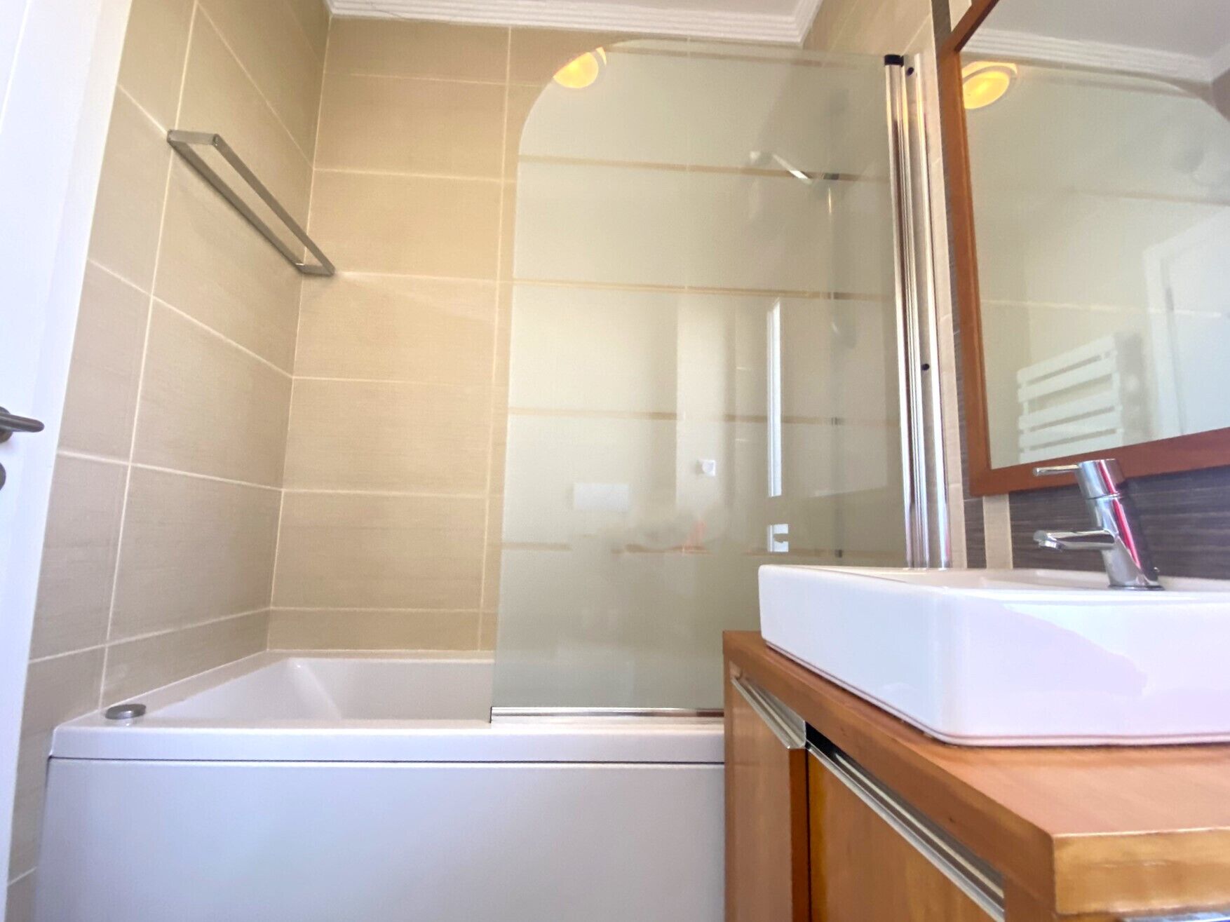A bathroom with a glass-enclosed shower, a white bathtub, and a wooden vanity with a white sink.
