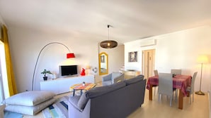 Un salon moderne avec un canapé gris, une table à manger avec des chaises, un téléviseur et une lampe rouge.
