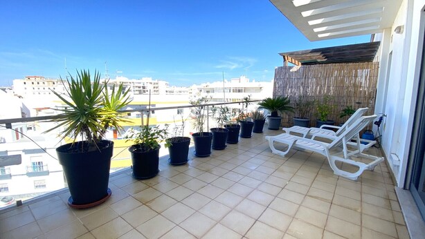 Un balcon agrémenté de plantes en pot, de chaises longues blanches et offrant une vue sur les immeubles.