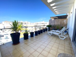 A balcony with potted plants, white lounge chairs, and a view of buildings. - Olhão Stylish by Homing (Olhao)