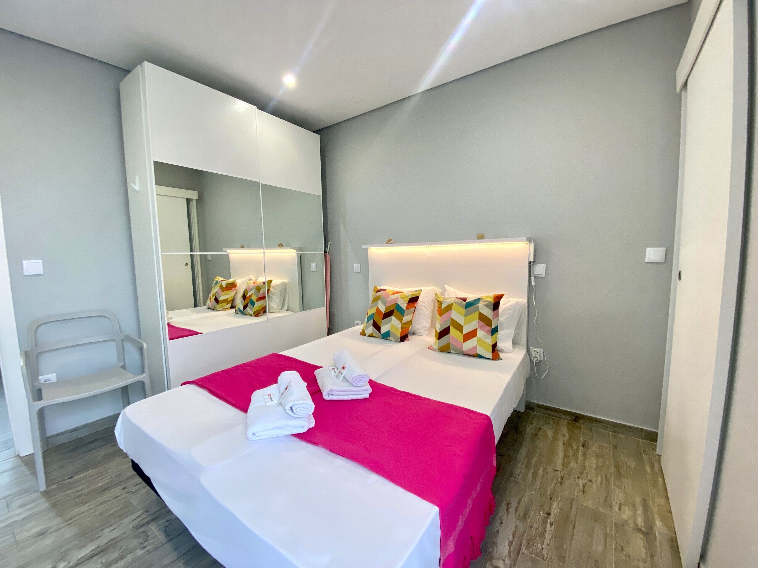 Quarto de hotel moderno com uma cama grande, um espelho e uma cadeira.