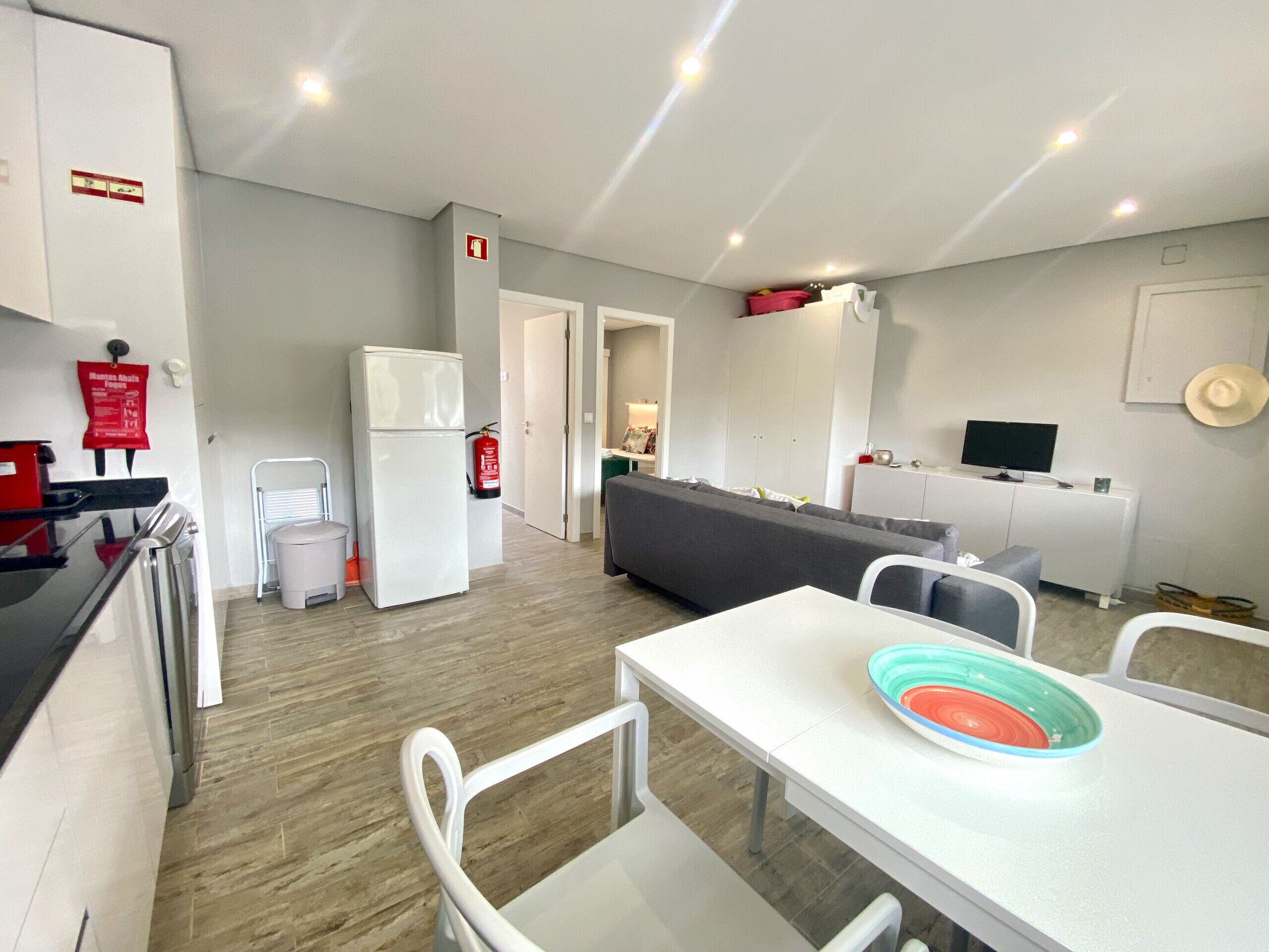 Una cocina moderna con armarios blancos, un refrigerador y un comedor con mesa y sillas.