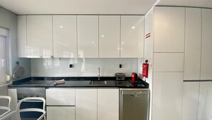 Une cuisine moderne avec des meubles blancs, un plan de travail noir, un lave-vaisselle et une machine à café.