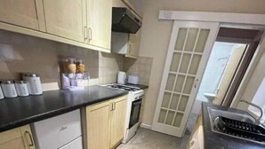Una cocina compacta con armarios de madera clara, encimera negra, horno integrado y ventana con vistas.