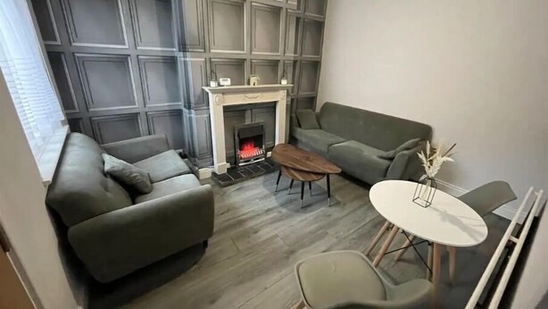 Una sala de estar moderna con chimenea, sofás grises, una mesa de centro y un comedor con una mesa y sillas blancas.