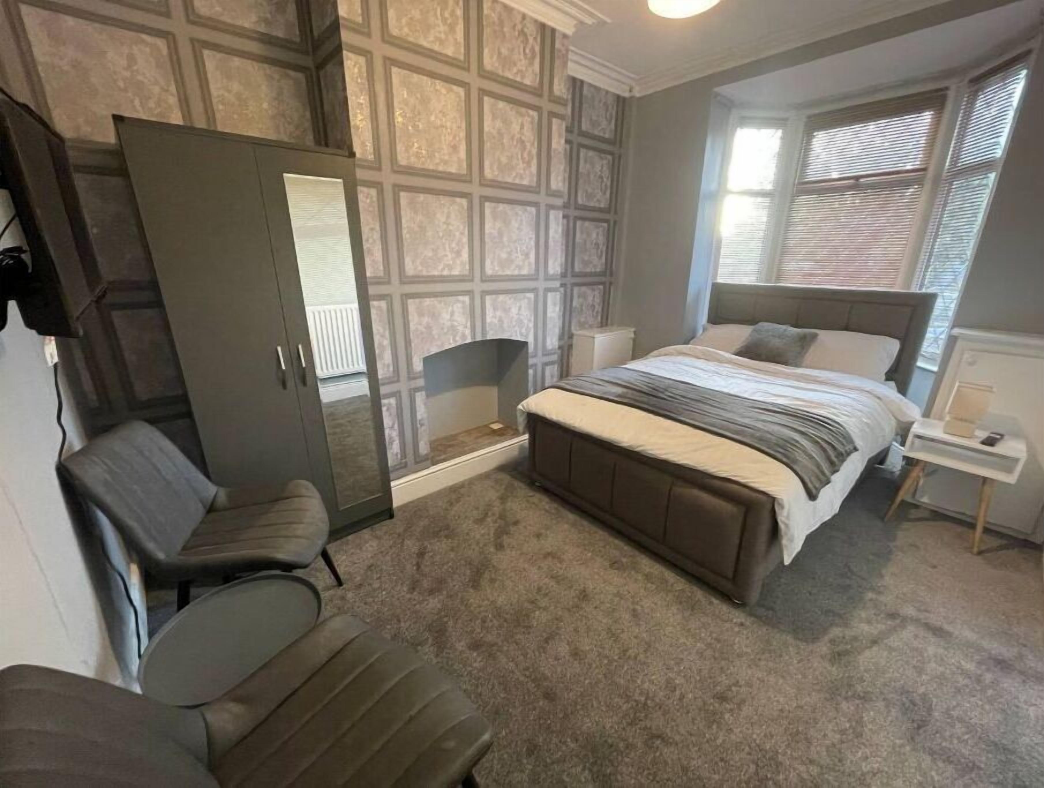 Ein Schlafzimmer mit einem großen Bett, einem Kleiderschrank, einem Sessel und einem Nachttisch.