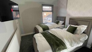 Habitación de hotel con dos camas, un televisor montado en la pared y una ventana con persianas.