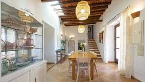 Un comedor amplio con una mesa y sillas de madera, una vitrina de vidrio con cerámica y una escalera que lleva a otro nivel.