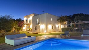 Una villa moderna con piscina, mobiliario de exterior e iluminación arquitectónica destacada.