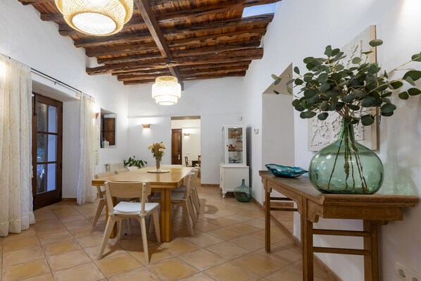 Un comedor con una mesa y sillas de madera, un florero verde con plantas y un techo de madera con vigas a la vista.