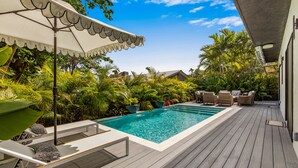 Ein Pool mit Liegestühlen und Sonnenschirmen, umgeben von üppiger Vegetation und einer Holzterrasse.