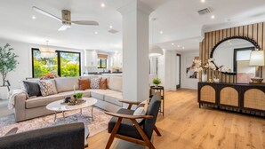 Ein modernes Wohnzimmer mit einer Couch, einem Couchtisch und Sesseln, ein Essbereich mit einer Holzkommode und eine Küche im Hintergrund.