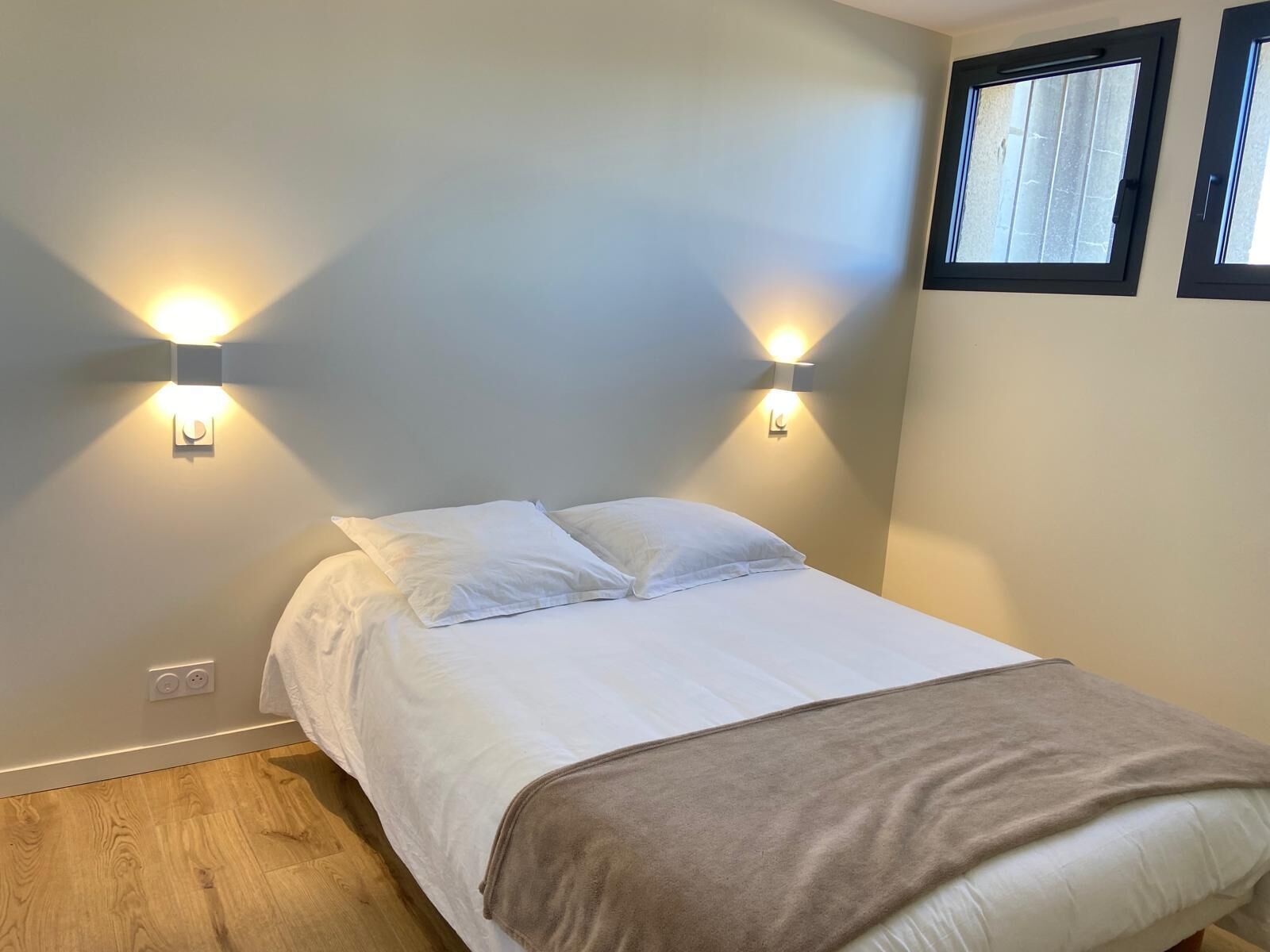 Un dormitorio con cama, dos luces empotradas, una ventana y piso de madera.