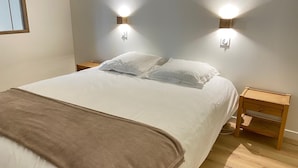 Un lit bien fait, recouvert d’une couverture marron, avec deux oreillers blancs et deux tables de chevet dotées de lampes fixées au mur.