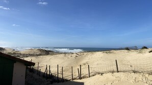 Une vue sur la plage, avec un paysage sablonneux, une clôture en bois et un bâtiment doté d’un toit végétalisé.