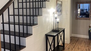 Un escalier avec des rampes noires et des murs blancs, une petite table avec une lampe et un plancher en bois.