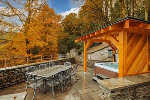 An outdoor patio with stone walls, a wooden pergola, a hot tub, and metal chairs. - Gate House (Coniston)