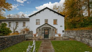 A white building with a stone entrance, a stone wall, and a grassy lawn.