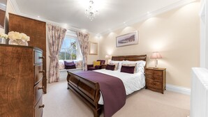 A bedroom with a large bed, a wooden dresser, a nightstand, and a window with curtains.
