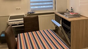 Et lille køkken med gasblus, indbygget ovn, et vindue med skodder, en lille vask og en opvaskemaskine.