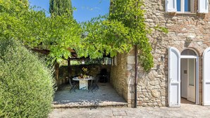 Un bâtiment en pierre doté d’un espace extérieur couvert avec des sièges, une table avec des chaises et un mur en pierre.
