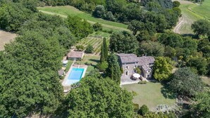 Vue aérienne d’une propriété comprenant une piscine, une maison en pierre et un jardin luxuriant.