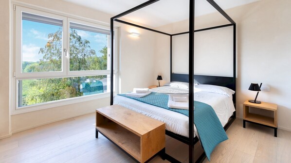 A four-poster bed with a view of trees through the window.