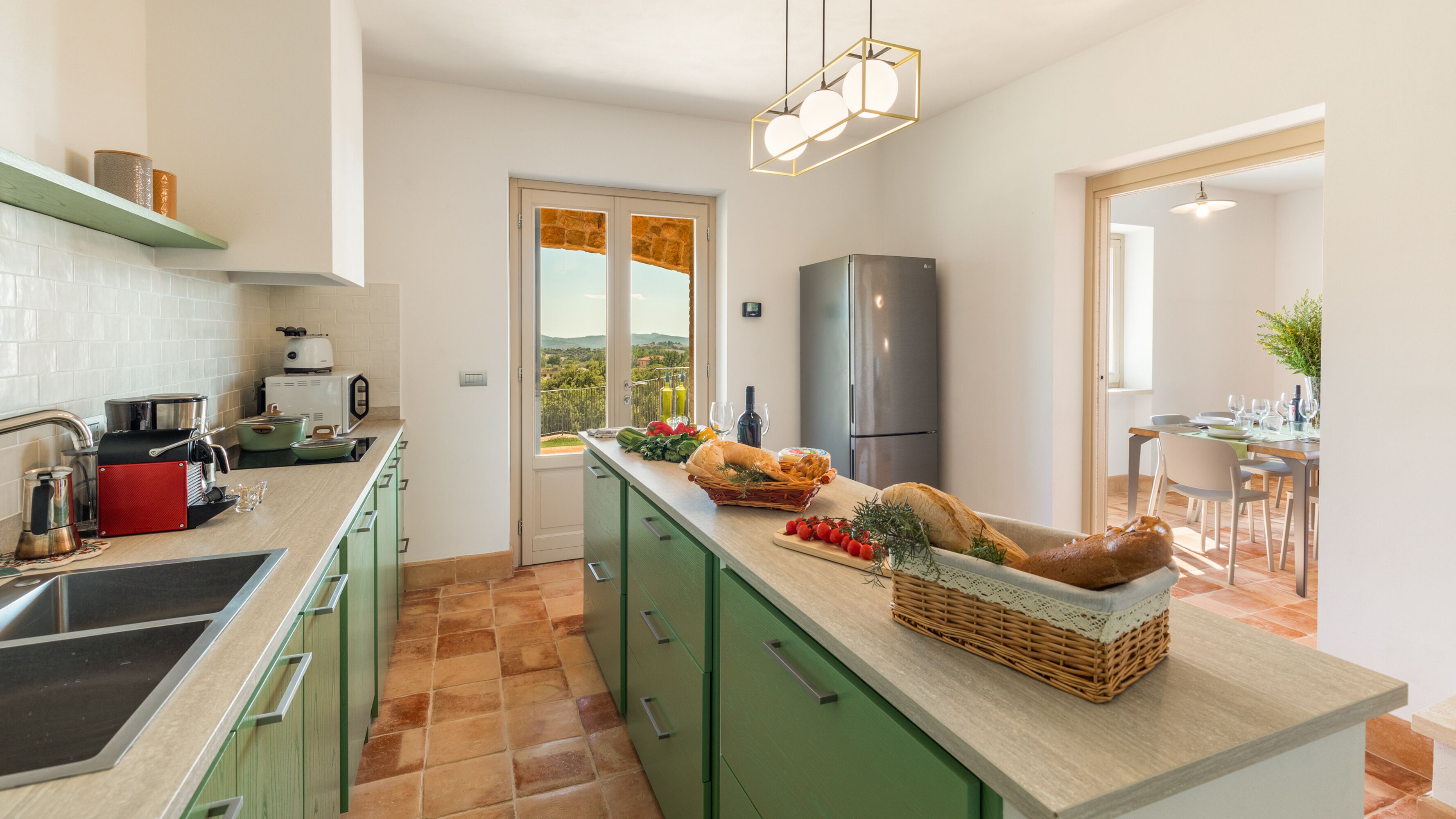 Eine moderne Küche mit grünen Schränken, einer großen Kochinsel mit frischem Obst und Gemüse, einem eingebauten Backofen und Blick durch die Tür.