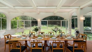 A dining area with a long table set for six, surrounded by large arched windows offering a view of a lush garden. - Villa Manganelli 12, Emma Villas (Camaiore)