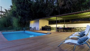 A swimming pool with a wooden deck, lounge chairs, a covered patio area, and a view of the surrounding forest. - Villa Manganelli 12, Emma Villas (Camaiore)