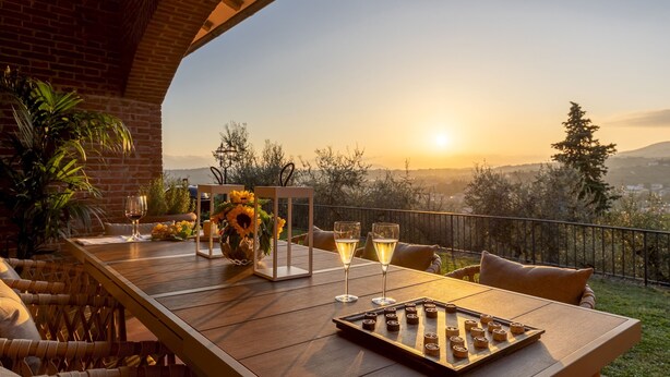 Une table à manger dressée avec des verres à vin et un jeu de société, offrant une vue panoramique sur un paysage magnifique, avec des montagnes et des arbres.