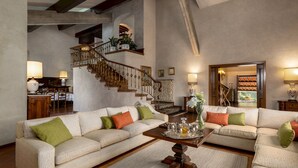 Un salon spacieux avec deux canapés beige, une table basse en bois et un escalier doté de rampes décoratives.