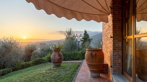 Une terrasse agrémentée de pots en terre cuite, un mur de briques et une vue sur des collines lointaines au coucher du soleil.
