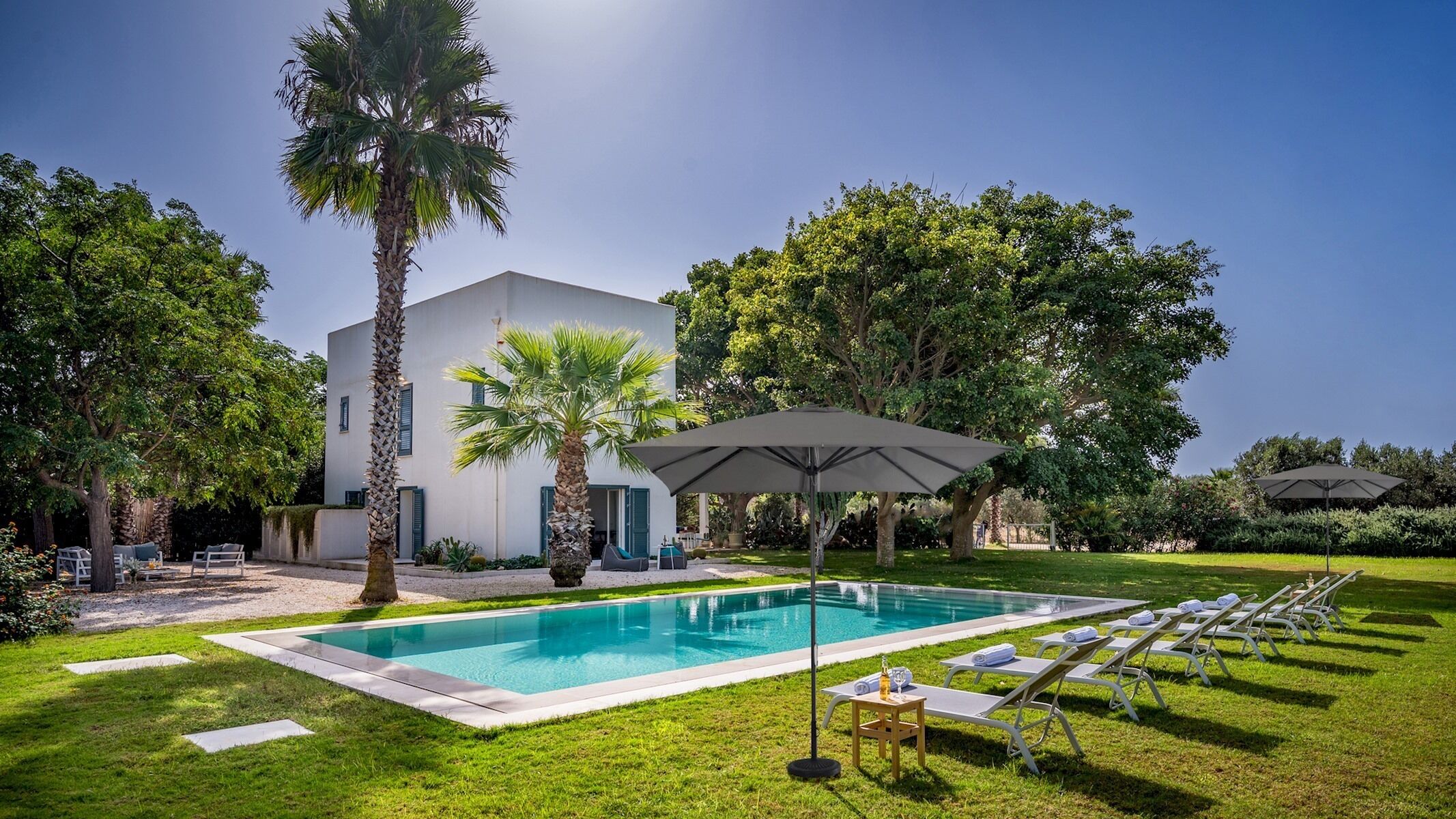 A modern house with a swimming pool, surrounded by lush greenery and palm trees.